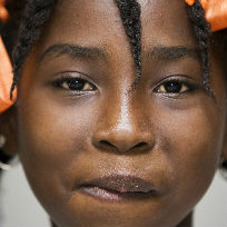 Criança negra sorrindo de frente para a câmera com laços laranjas no cabelo / Foto: UN Photo/Marco Dormino CC BY-NC-ND 2.0