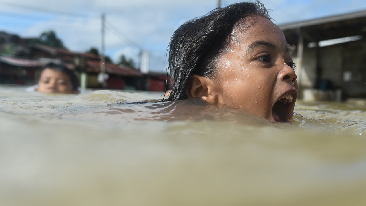 Menina nadando em água aparentemente suja e com a boa aberta pedindo ajuda