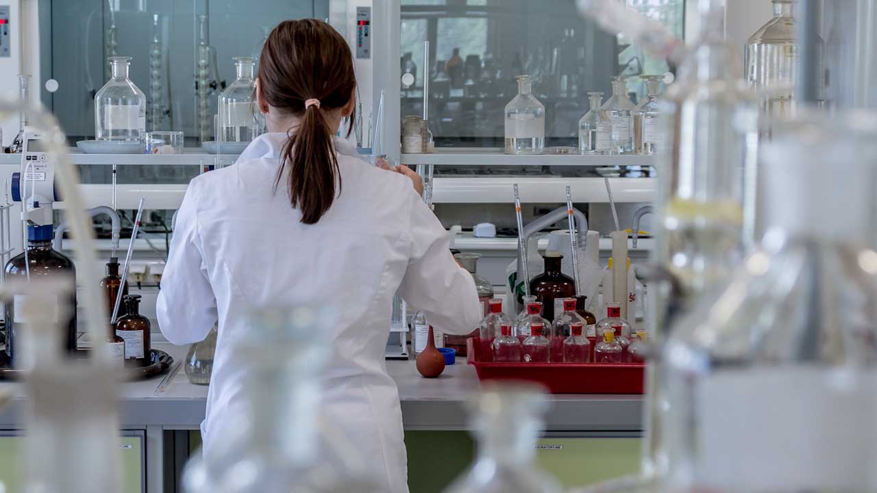 Pessoa com jaleco de cientista de costa em um laboratório