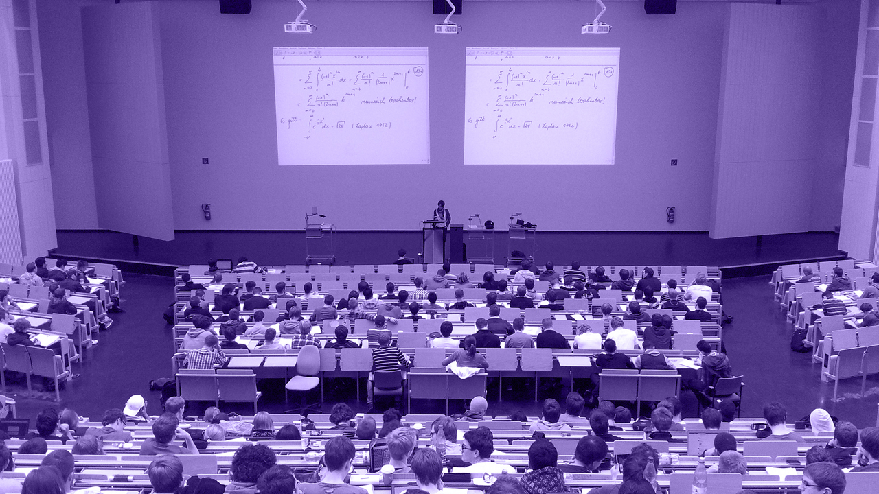 Foto de um auditório com muitos alunos e um professor dando aula no palco