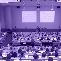 Foto de um auditório com muitos alunos e um professor dando aula no palco