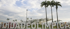 Na frente da imagem uma escultura interativa com a frase cidade olímpica com duas palmeiras atrás do lado direito e o Museu do Amanhã no plano de fundo