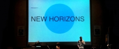 Nosso pesquisador do Observatório do Amanhã, Davi Bonela, em um palco de um auditório apresentando seu projeto. Ao fundo uma tela escrito "New Horizons".